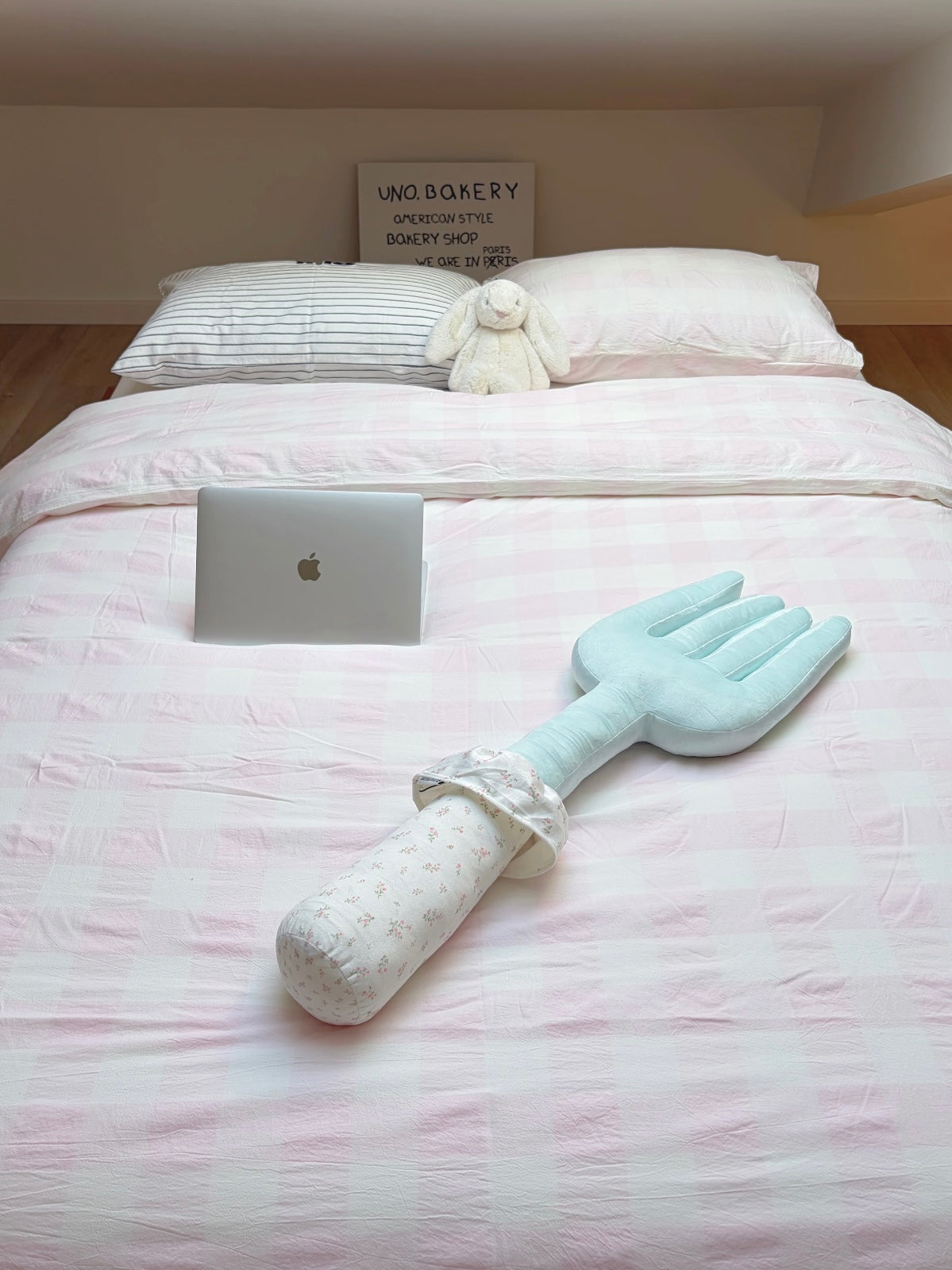 A blue fork pillow lies across pale bedding, with a floral handle and gathered collar below the fork head.