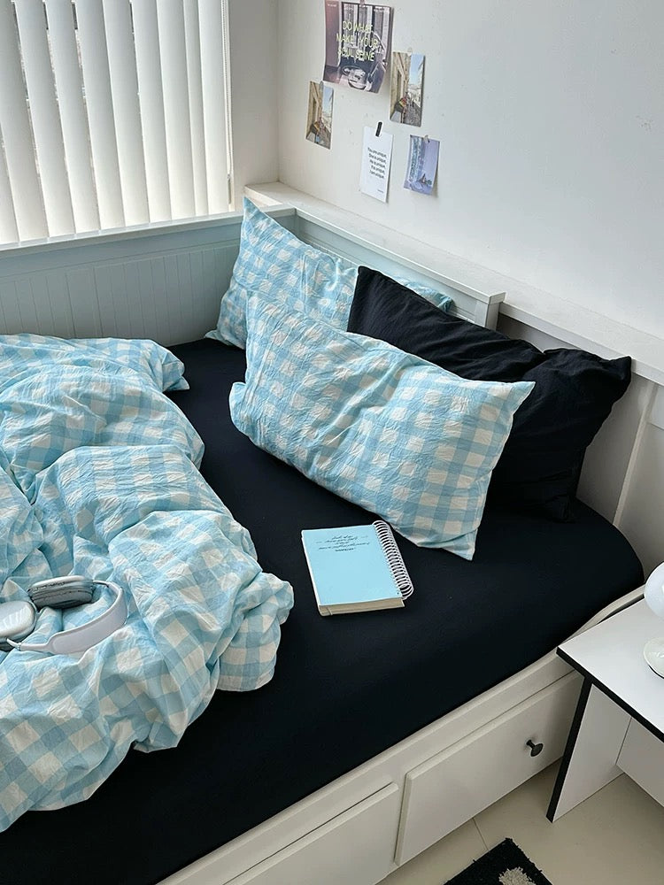 Bed with blue checkered bedding and pillows in a room with a window and desk.