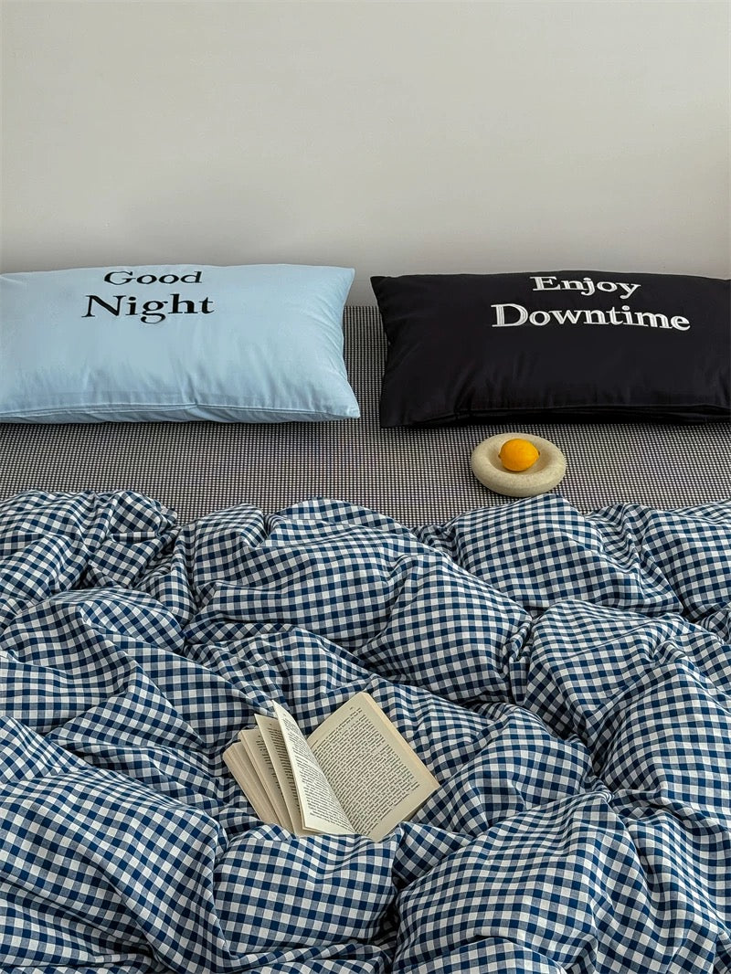 Bed with checkered duvet, pillows with text, and a book on a gray surface.