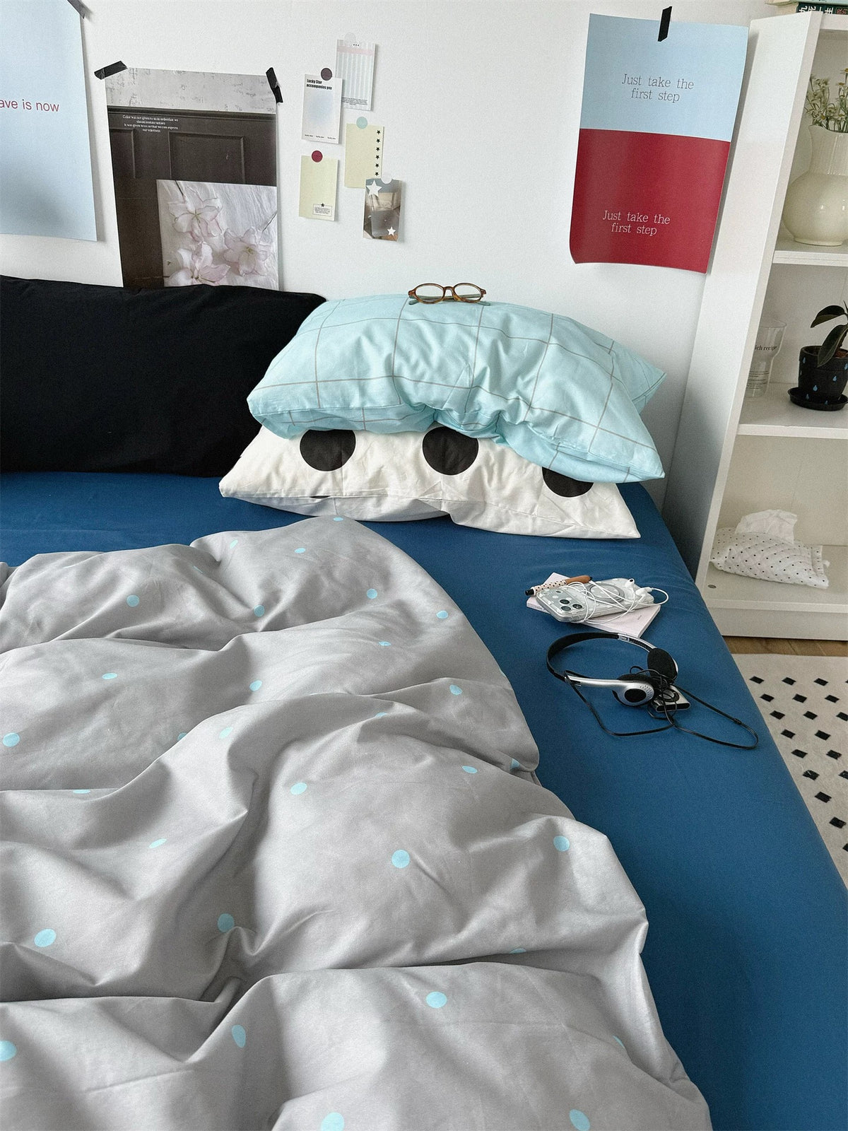 Blue and gray bedding with a black pillow beside stacked check and dot pillowcases.