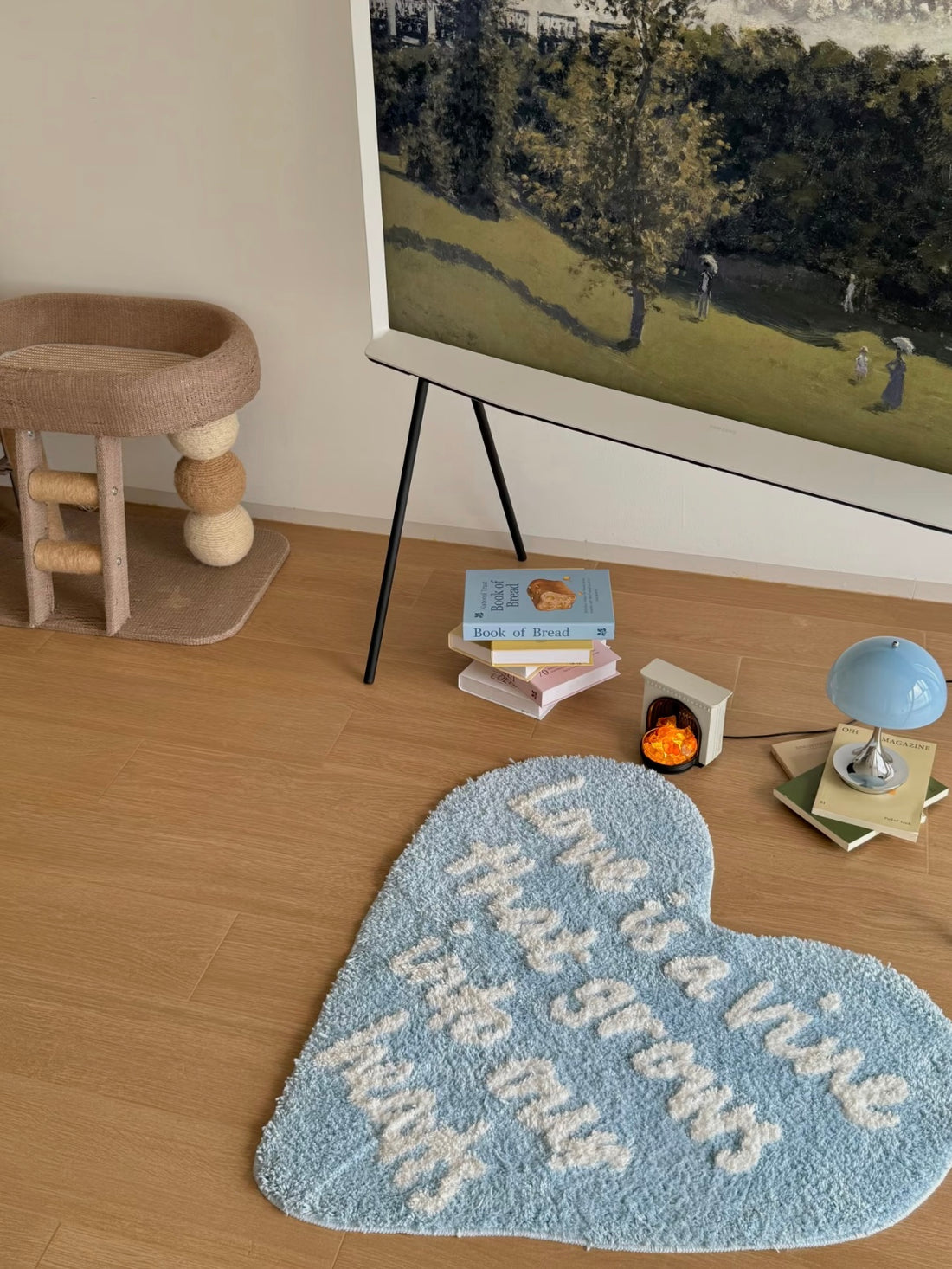 Blue heart rug with white lettering lies on a wooden floor, with books and a small blue lamp nearby.
