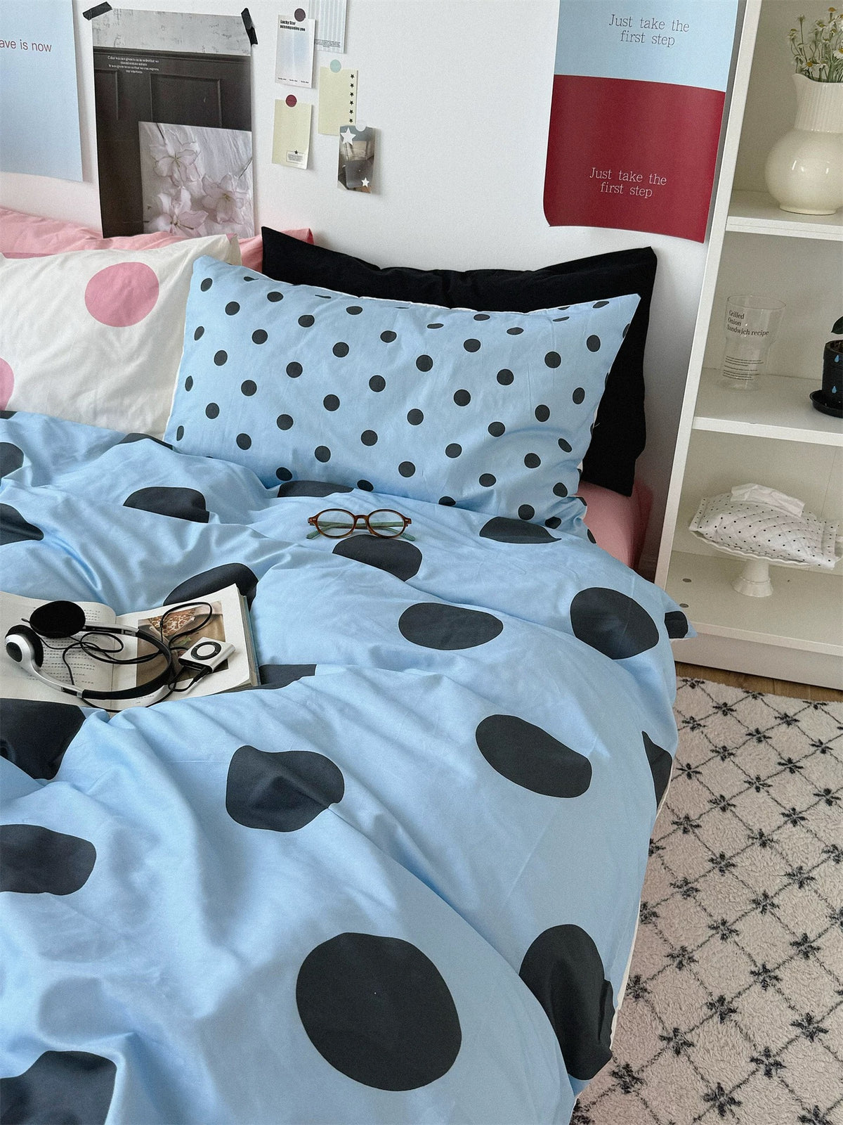 Large black dots on the blue cover contrast with the smaller dots on a blue pillowcase and pink dots on a cream pillowcase.