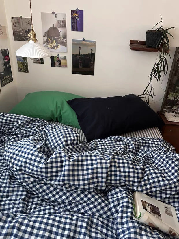 Bed with checkered duvet, green and black pillows, and photos on the wall.