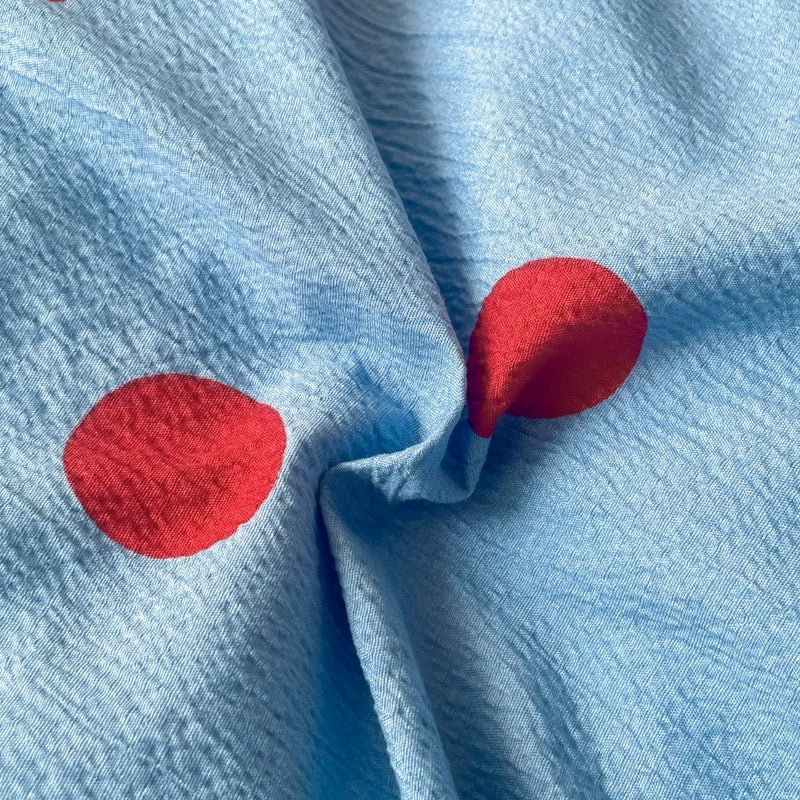 Polka dot bedding set in blue with red details styled for dorm room decor and preppy aesthetic interiors.