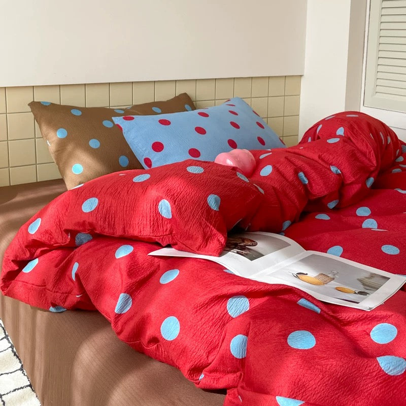 Red blue polka dot bedding set styled on preppy dorm bed with pillows natural light