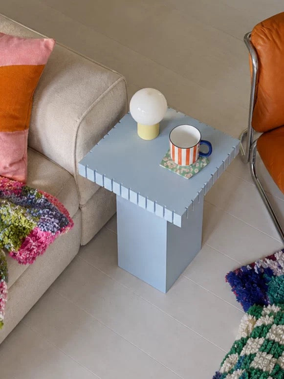Pastel blue side table with a striped edge top next to a beige sofa and an orange leather chair