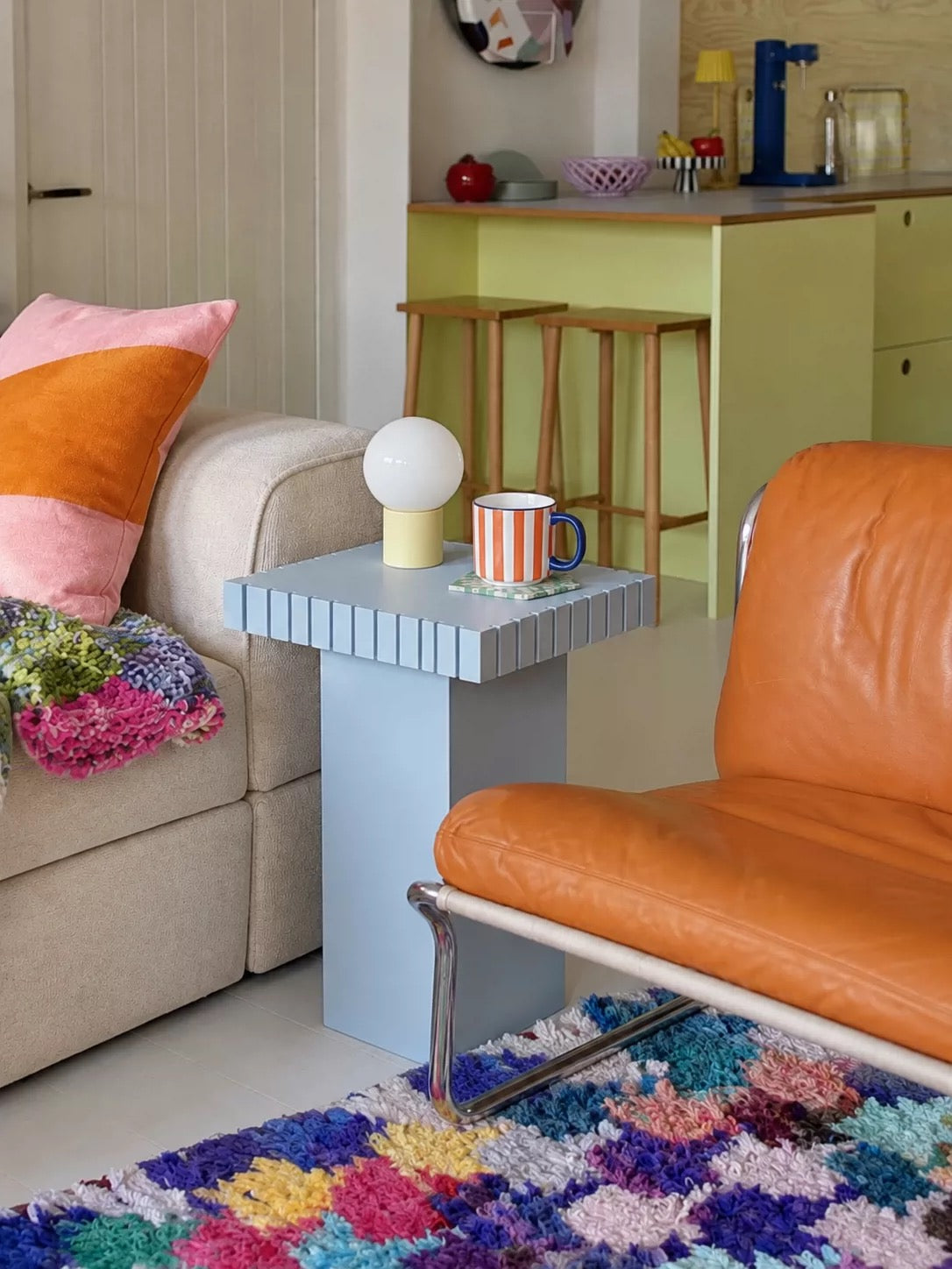 Blue small side table with vertical stripes on the top edge in a living room with green kitchen cabinets