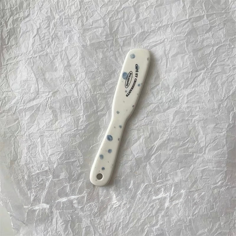 A white ceramic spatula with blue speckles and black printed text reading 'Craie et Comp' on a crumpled white paper background.