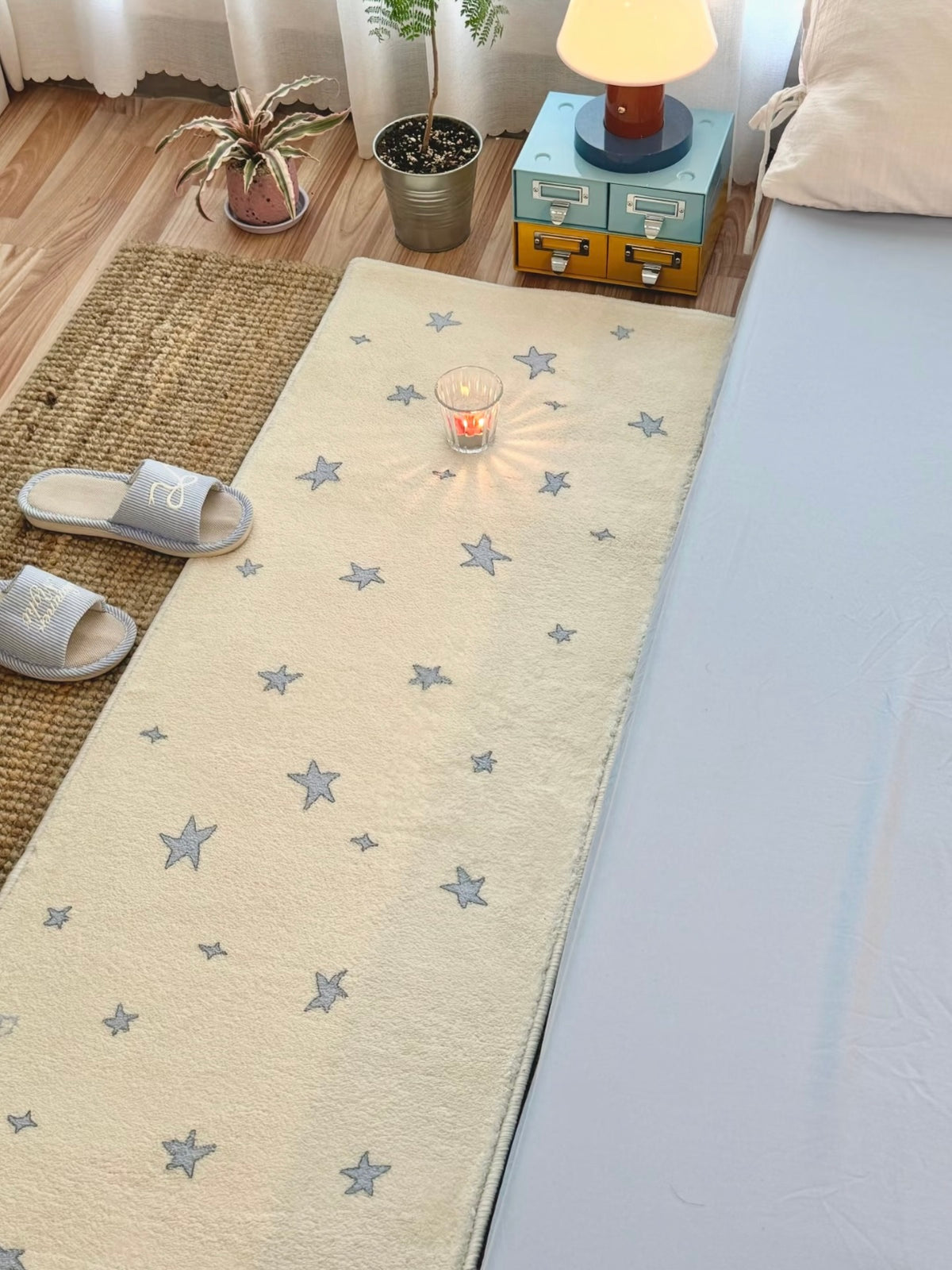 A blue star runner rug stretches along the side of a bed, with blue slippers near its left edge.