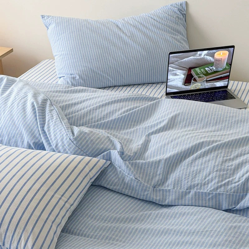 Soft blue striped duvet cover paired with matching pillowcases and flat sheet on minimalist wooden platform bed.