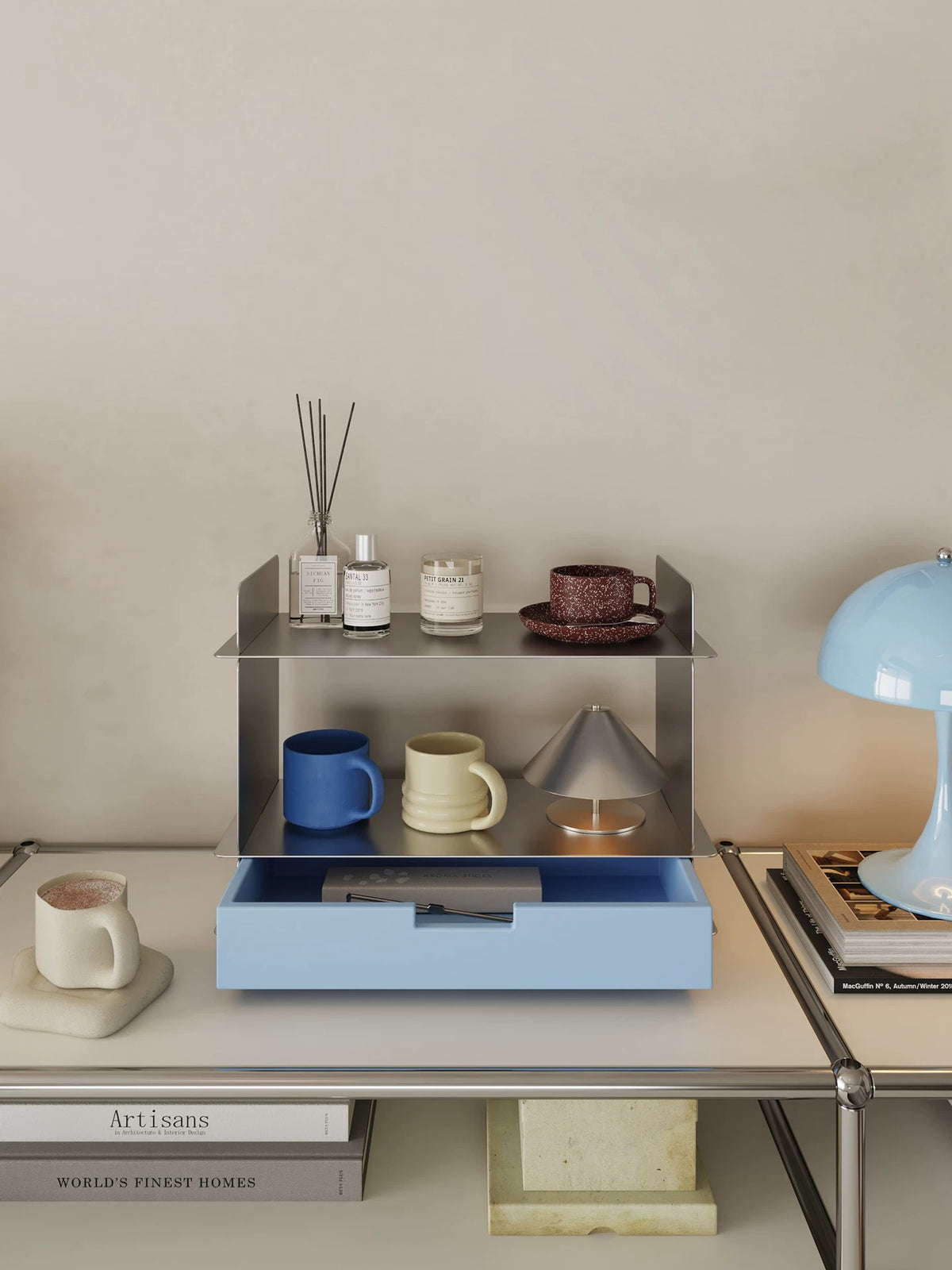 Blue tabletop shelf with a drawer next to a light blue lamp and a stack of books on a white console