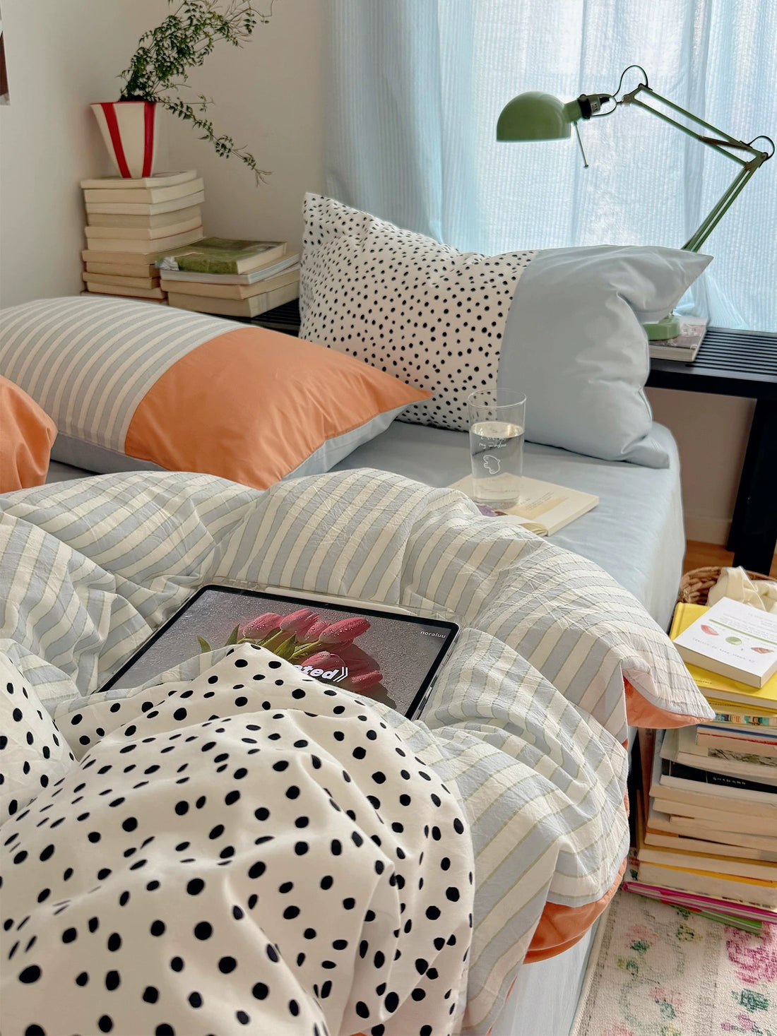 Pastel bedding combines a striped cover with dotted fabric folded forward and a tablet resting on the bed.