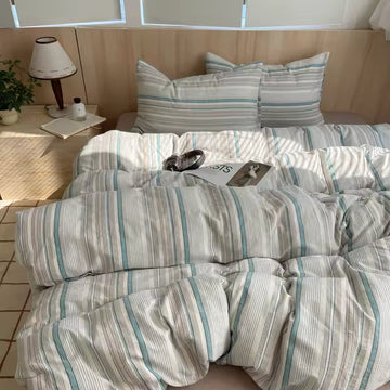 Blue striped cotton bedding set styled on minimal wood bed with neutral Nordic bedroom decor lighting