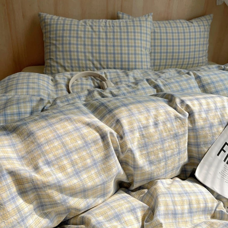 Plaid bedding set on a bed with pillows and a bag.