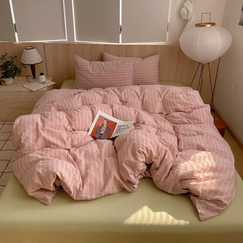 Bed with pink striped bedding and pillows in a room with a lamp and plant.