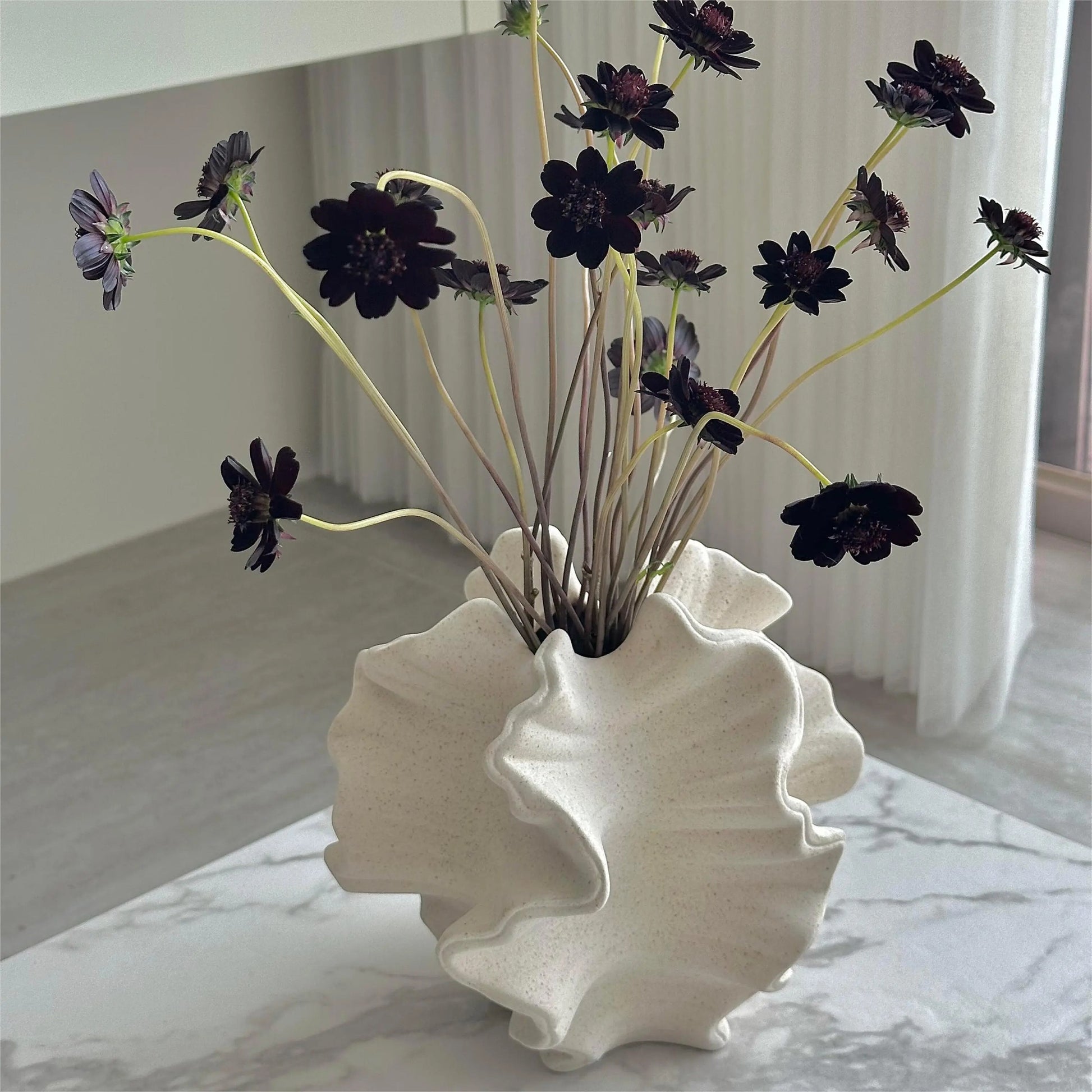 White shell-shaped vase with dark flowers on a marble surface
