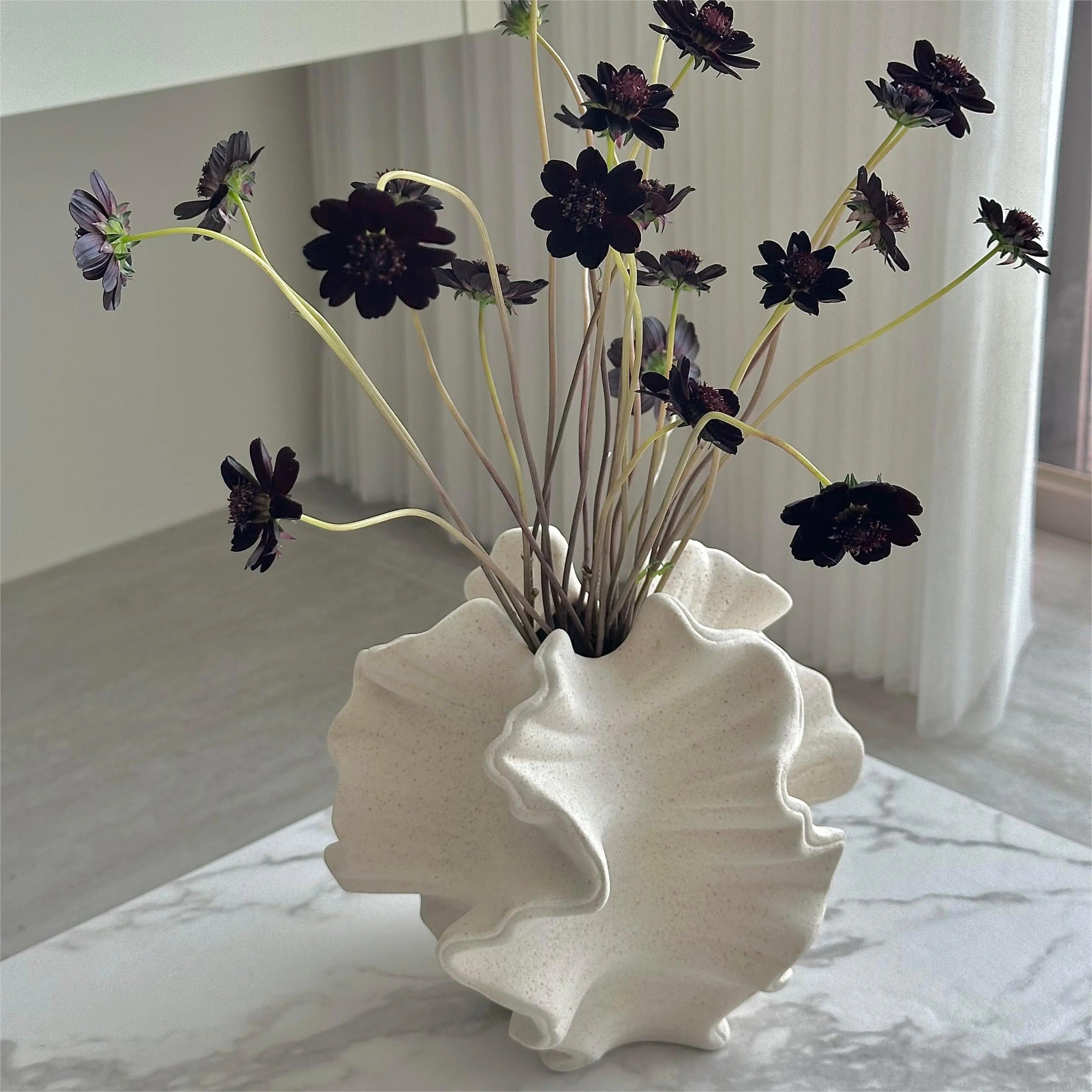 White shell-shaped vase with dark flowers on a marble surface