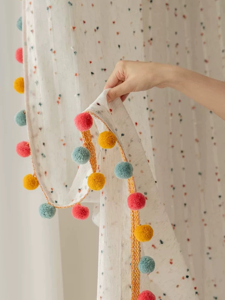 Decorative garland with colorful pom-poms held against a polka dot curtain.