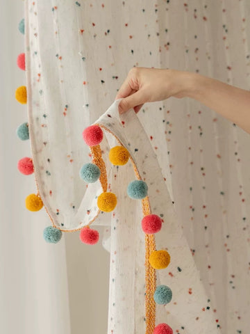 Decorative garland with colorful pom-poms held against a polka dot curtain.