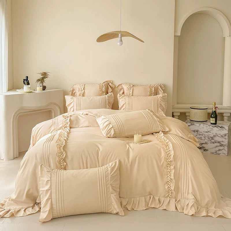 Beige ruffled bedding set on a bed in a softly lit bedroom.