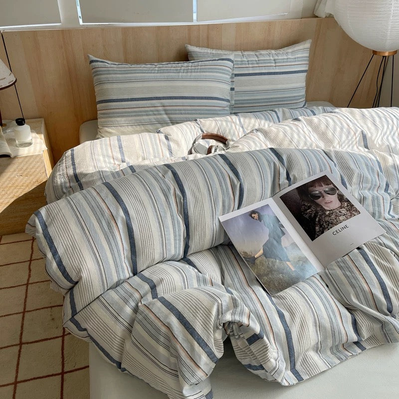 Bed with striped bedding and a magazine on a wooden floor.