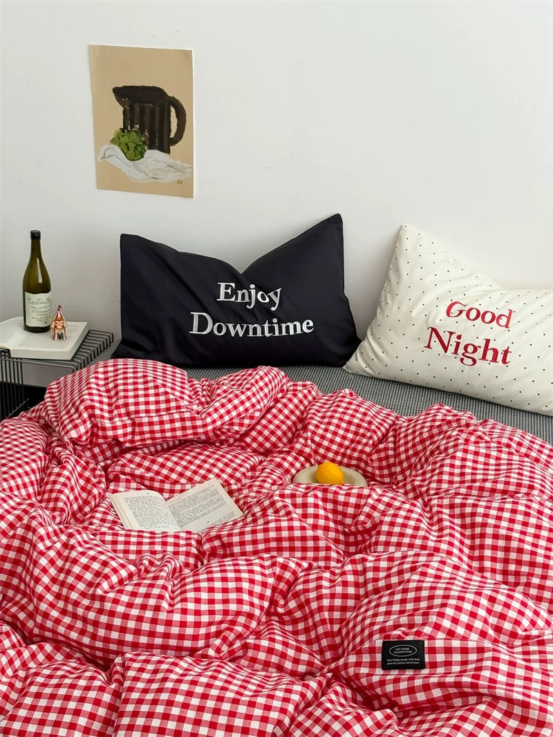 Red and white checkered comforter on a bed with pillows labeled 'Enjoy Downtime' and 'Good Night'.