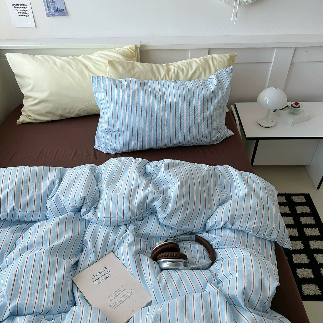 Bed with blue striped bedding and pillows, nightstand with lamp in the background