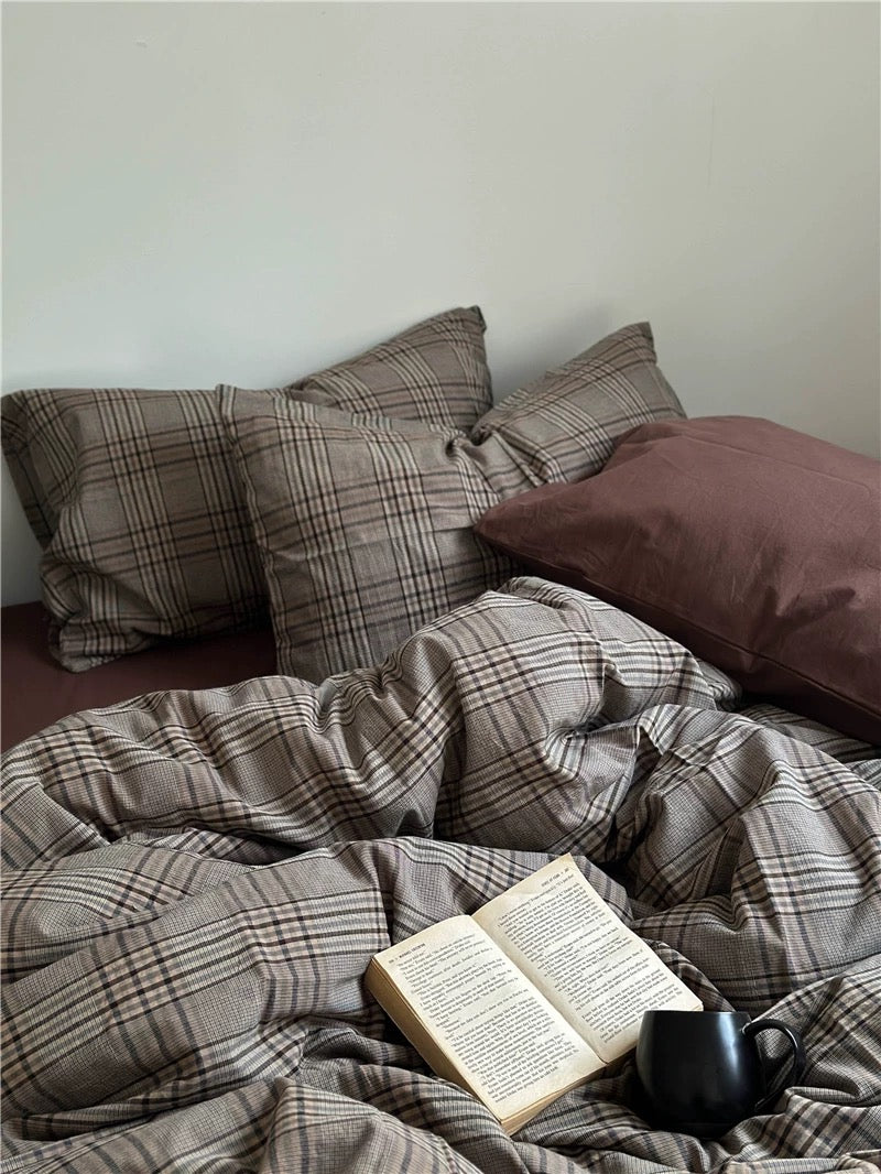 Plaid bedding with an open book and a mug on a bed.
