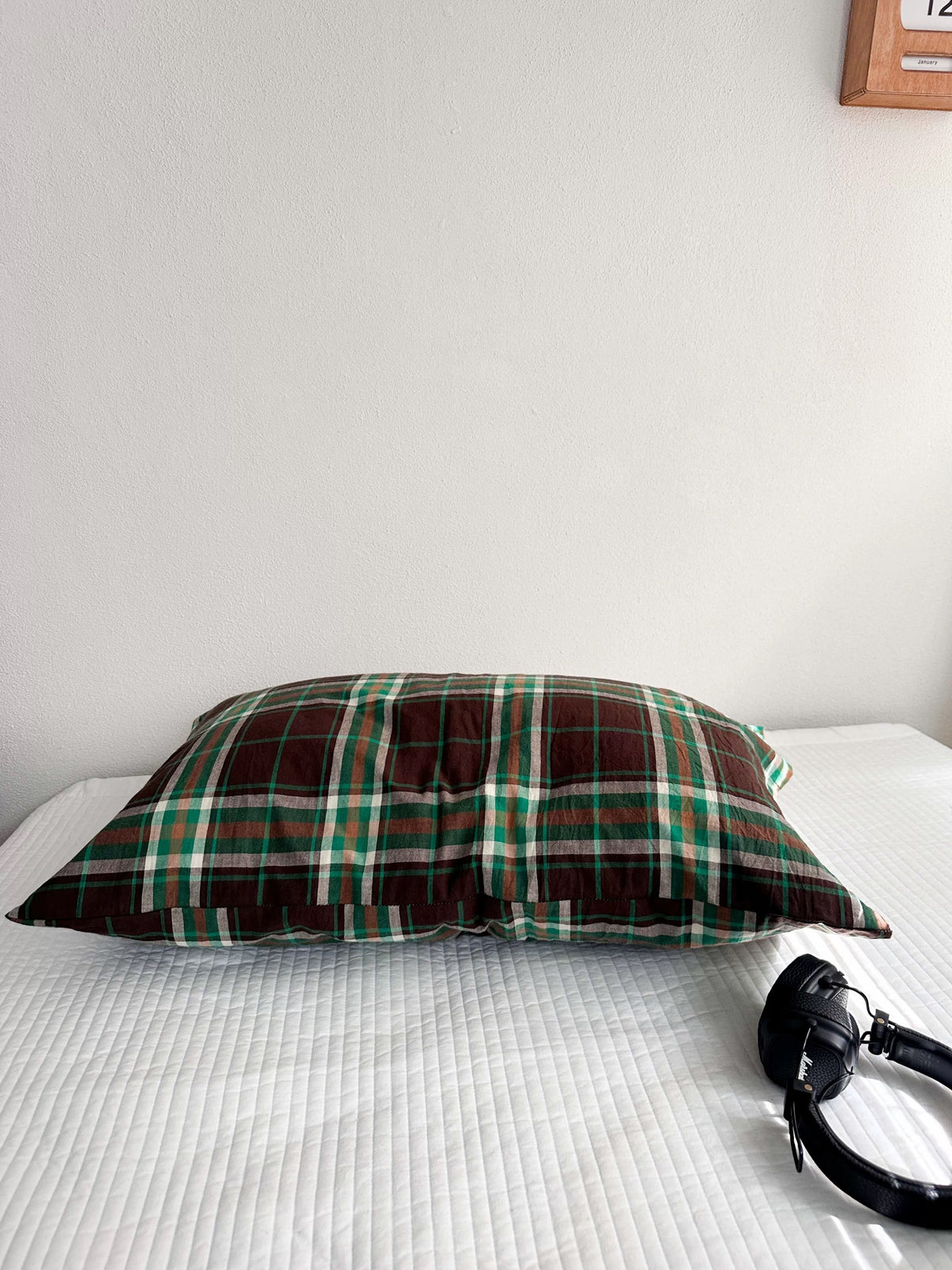 A brown and green tartan pillowcase is shown on its own, with thin light lines crossing the checks.
