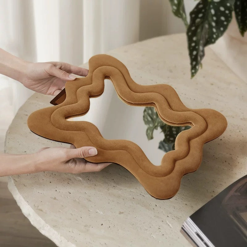 Person holding a wavy brown mirror on a light surface with a plant in the background