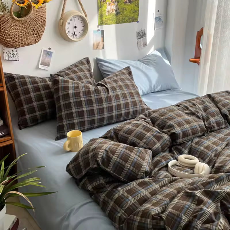 Bedroom with plaid bedding, pillows, and a yellow mug on a white bedspread.