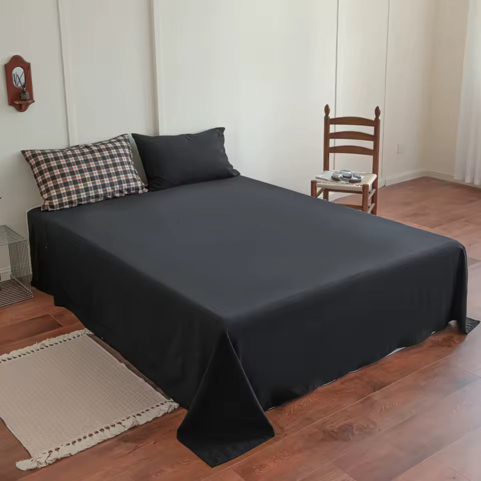 Bed with black fitted sheet and pillows in a room with wooden floor and chair.