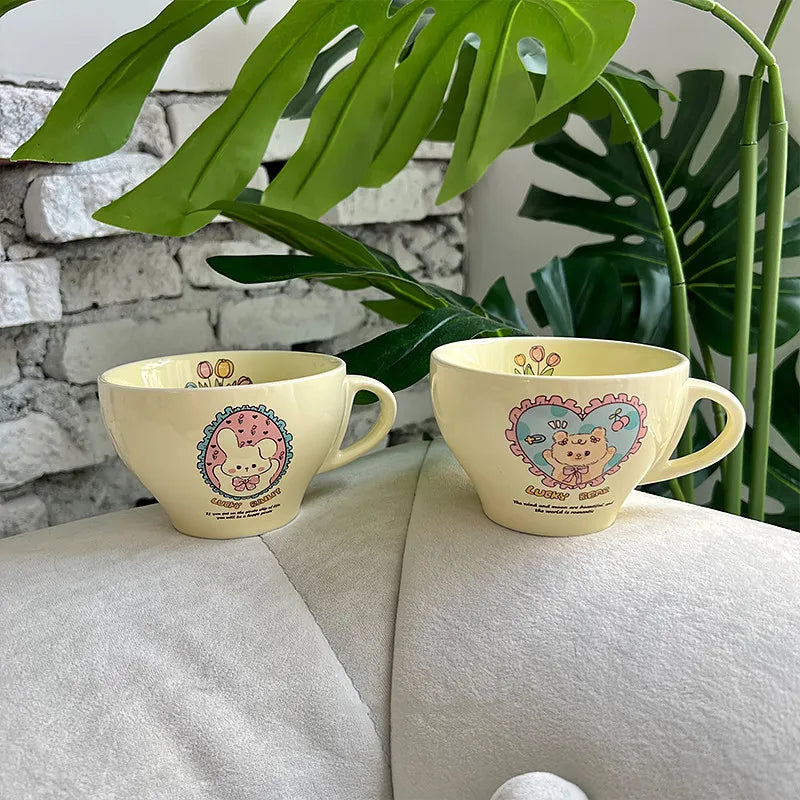 Two pastel yellow ceramic mugs with Sanrio character prints, displayed on a light beige sofa with green plant leaves and a white brick wall in the background.