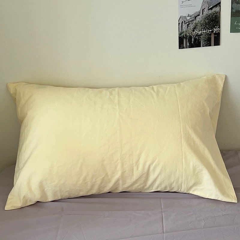 Single solid butter yellow cotton pillowcase on a bed.