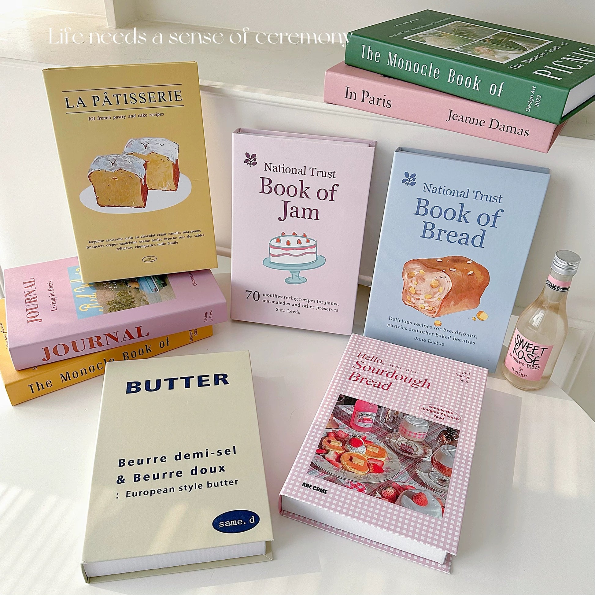 Collection of cookbooks on a white surface with a bottle of sweet wine.