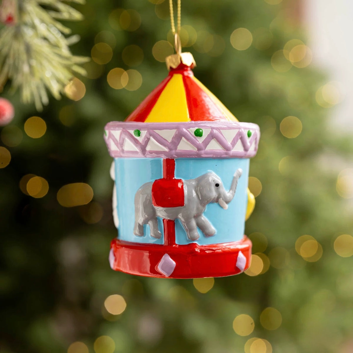 A carousel ornament has an elephant on a blue body beneath a red and yellow roof with lilac trim.