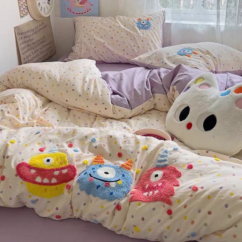 Children's bedroom with colorful bedding featuring cartoon monsters and a plush toy.