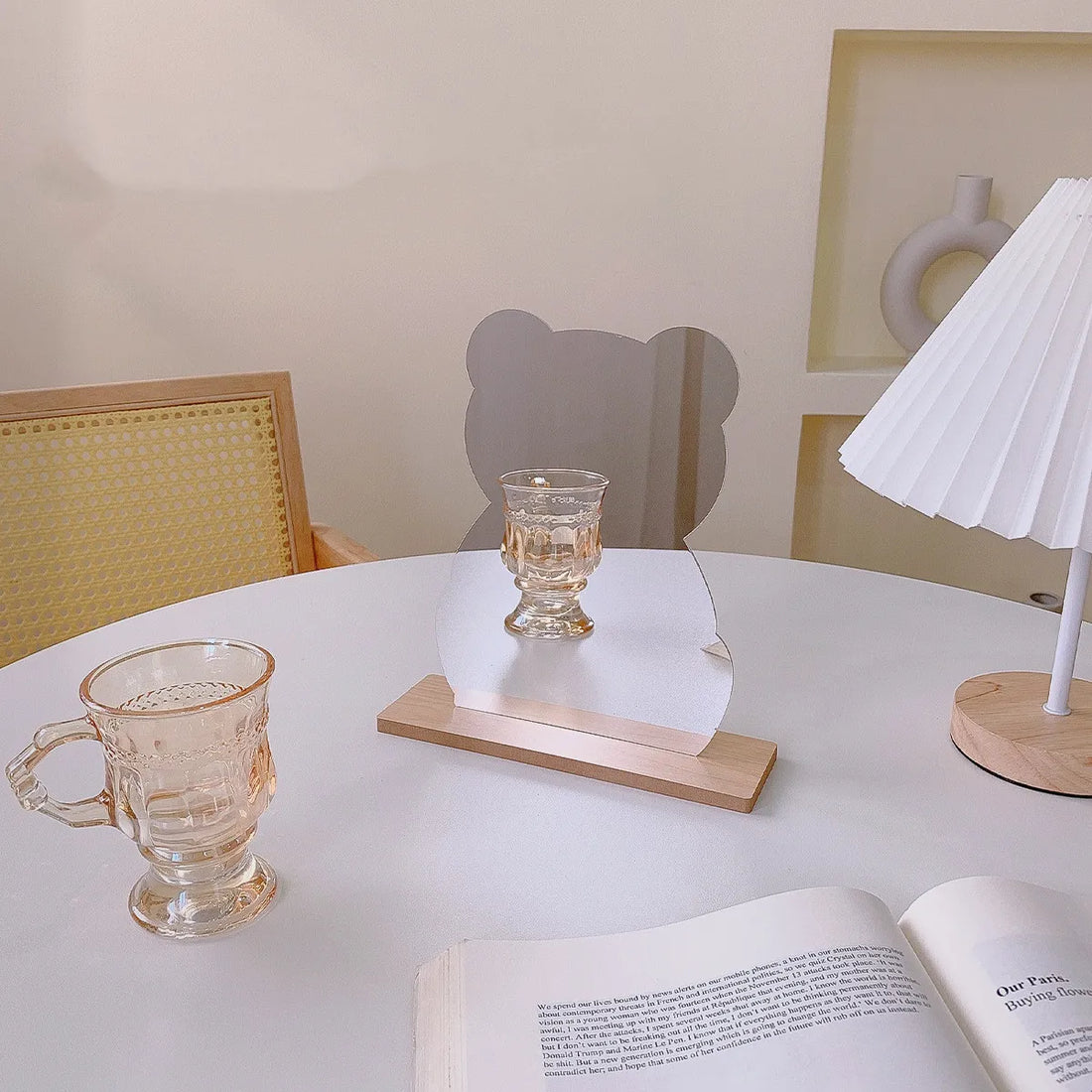 Two acrylic bear-shaped tabletop decor pieces with wooden bases on a white table, styled in a soft indoor setting with a small lamp, lace cloth, and glassware.