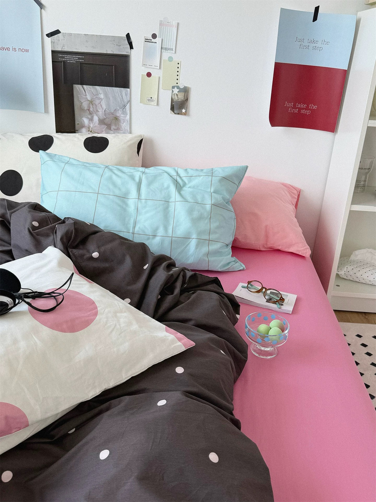 Side view of charcoal dotted bedding with a blue checked pillow, a plain pink pillow and a large black dotted pillow behind.