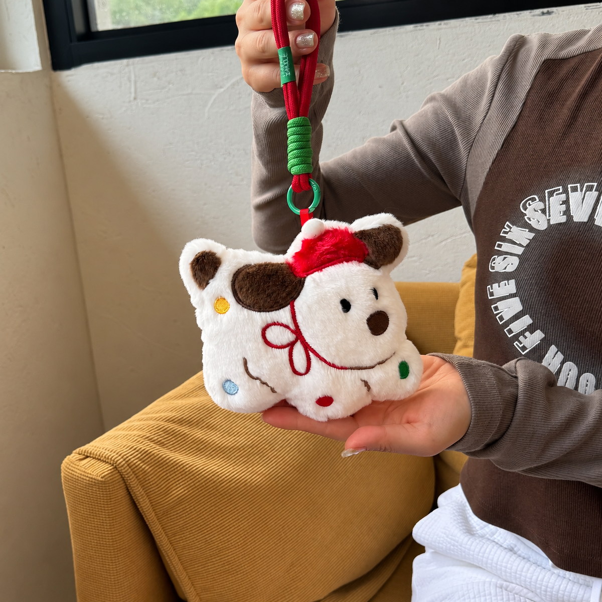 Small white Christmas puppy plush keychain with Santa hat held above a chair