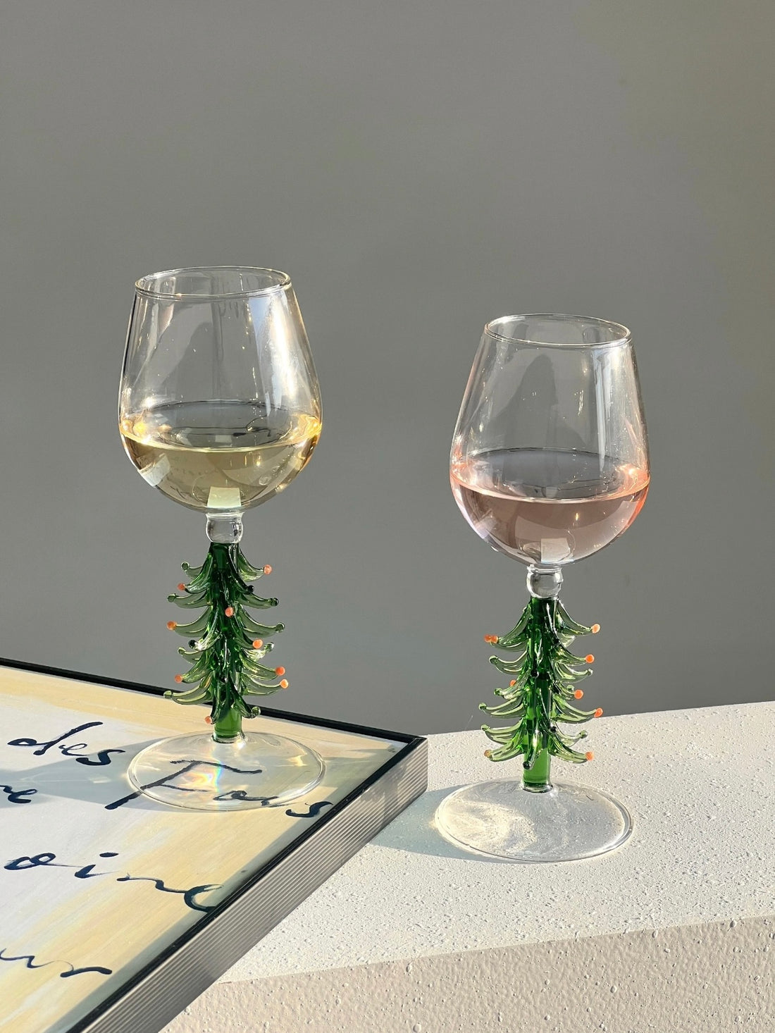Two Christmas tree wine glasses with green sculptural stems on a light table