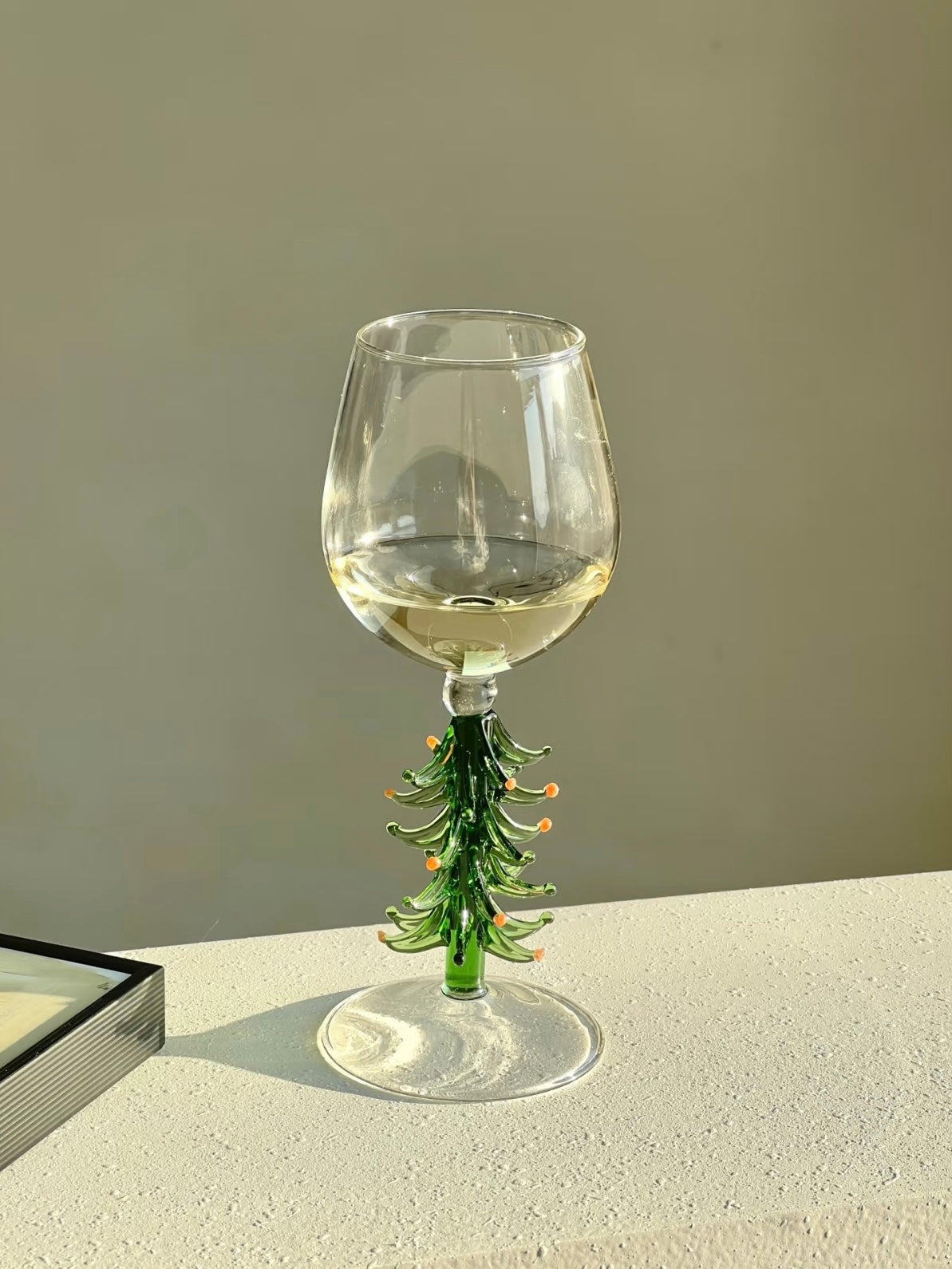 Single Christmas tree wine glass with green tree stem on a light surface