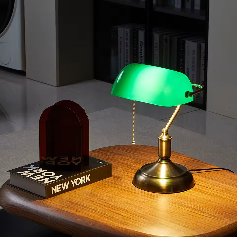 Vintage-style desk lamp with green glass shade on a wooden surface next to a book titled 'New York'.