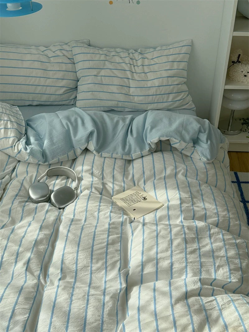 Bed with light blue striped bedding, a book, and headphones on a white wall background.