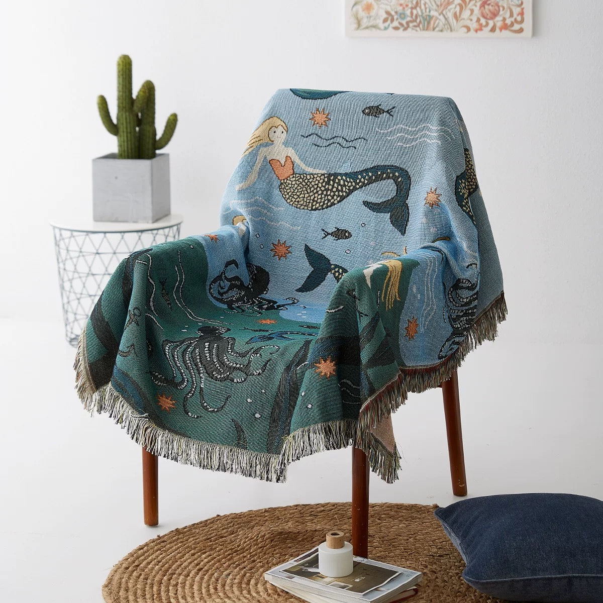 Mermaid-themed blanket draped over a chair in a room with a cactus and small table.