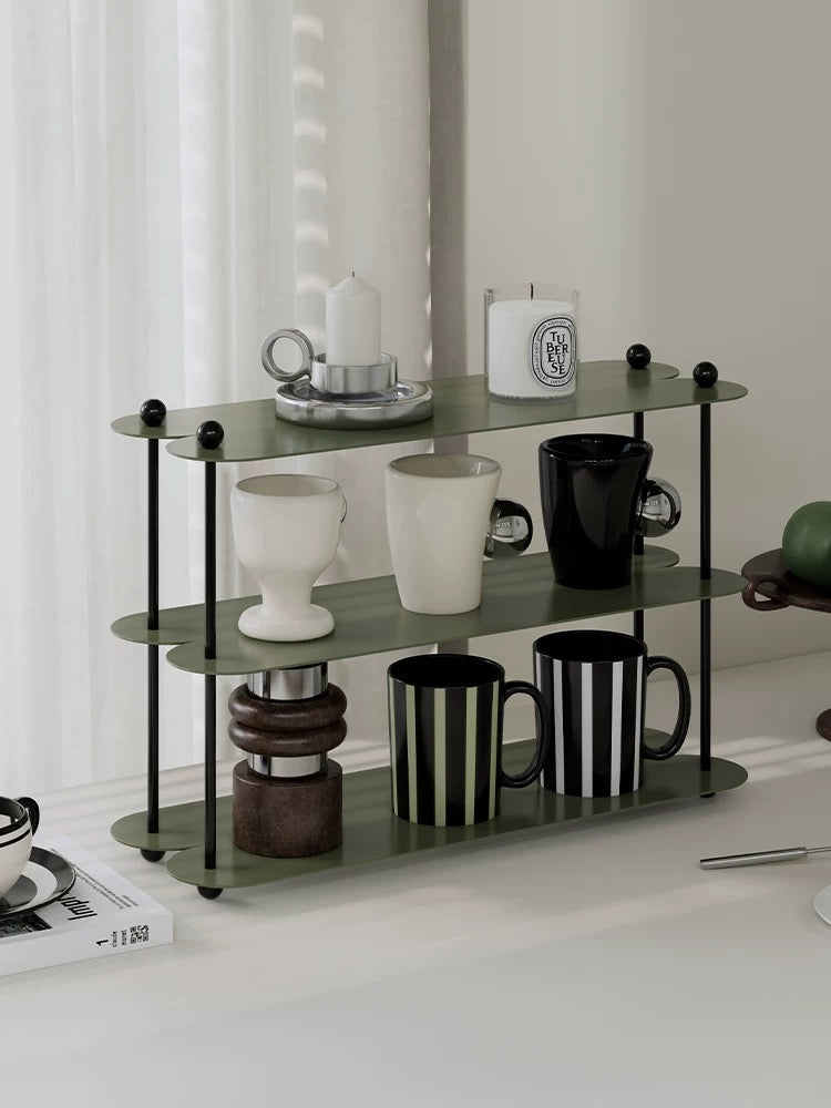 A green coffee mug shelf with black posts displays striped mugs below white and black cups on the middle tier.