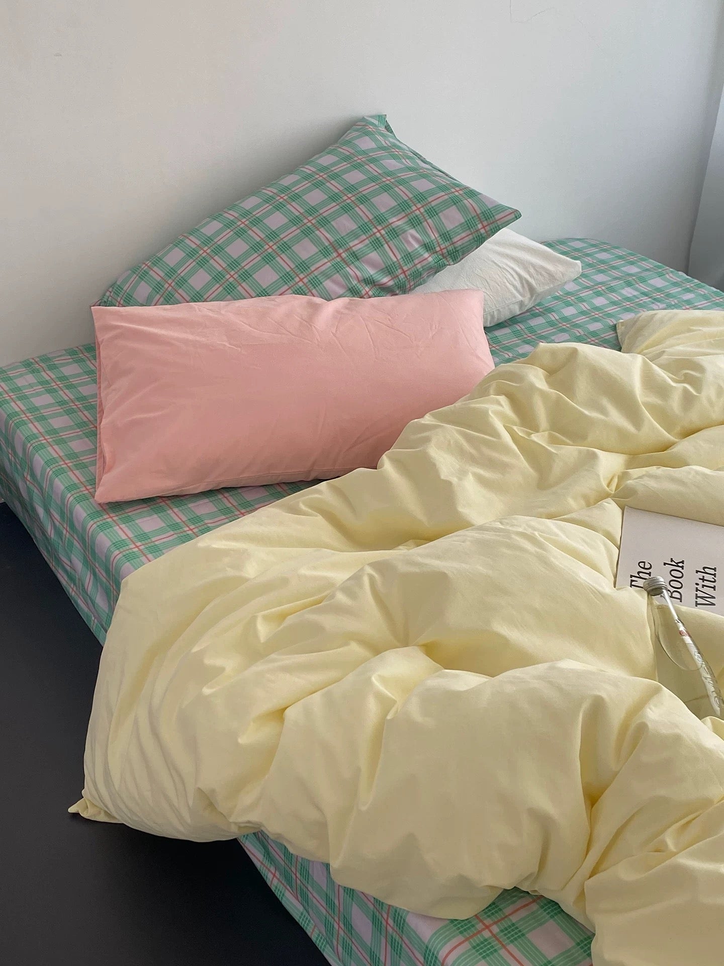 Bed with checkered green and white sheets, pink pillow, and yellow comforter.