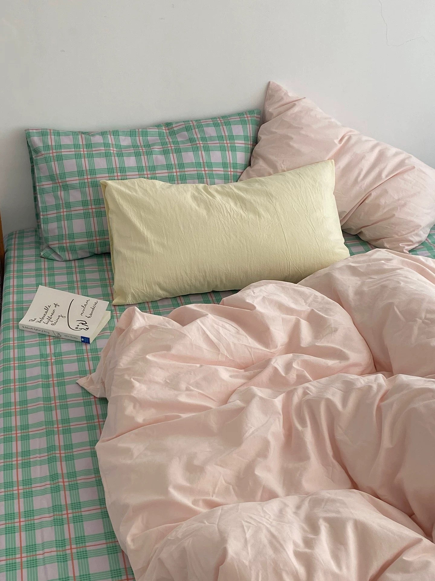 Bed with pink bedding and plaid pillows against a white wall