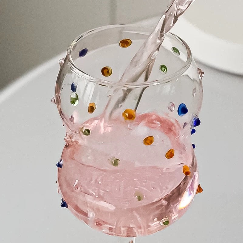 Glass with colorful dots being filled with pink liquid