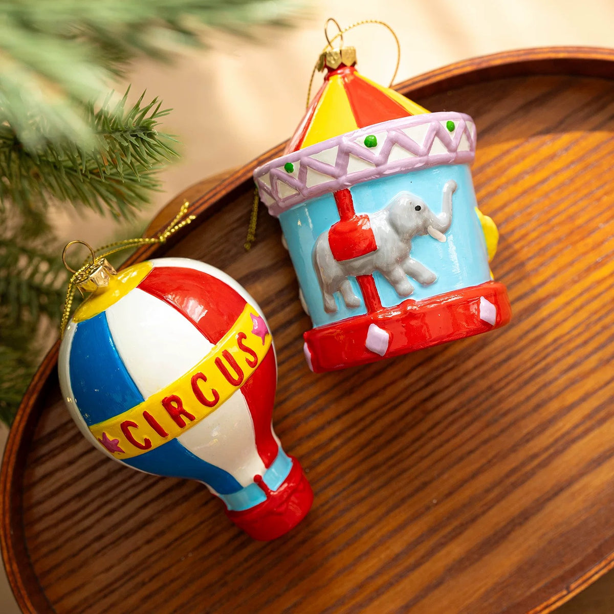 Colorful Christmas ornaments pair a striped hot air balloon with a blue elephant carousel and red roof.